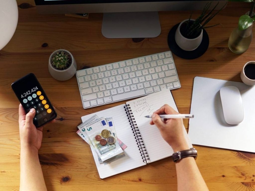 person budgeting with calculator, cash, and coins on desk while preparing documents to rent a house in the UK